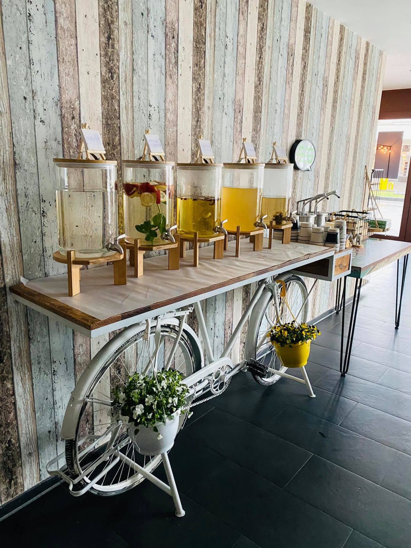 Fahrrad-Bar mit Glasspendern voller hausgemachter Limonaden vor einer Holzlattenwand