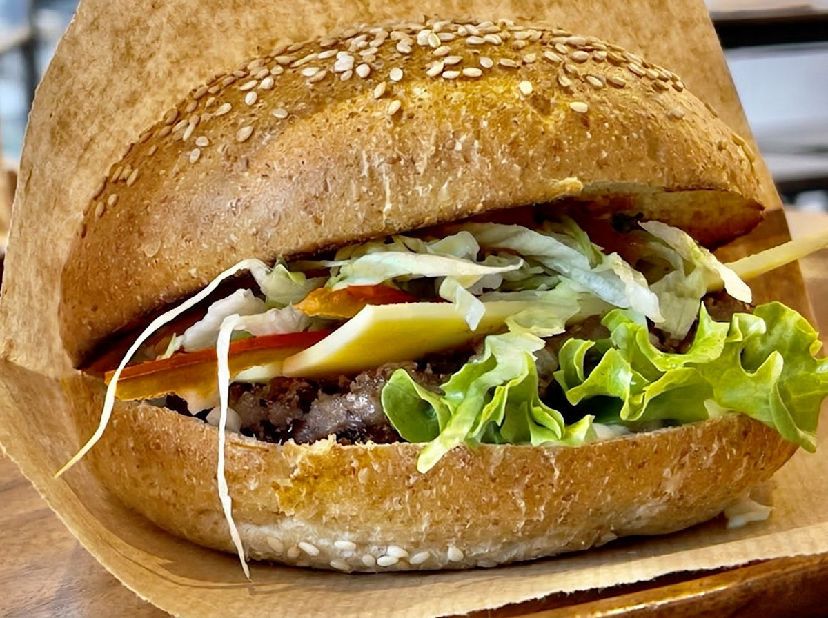 Nahaufnahme eines Sesambuns mit Salat und veganem Käse