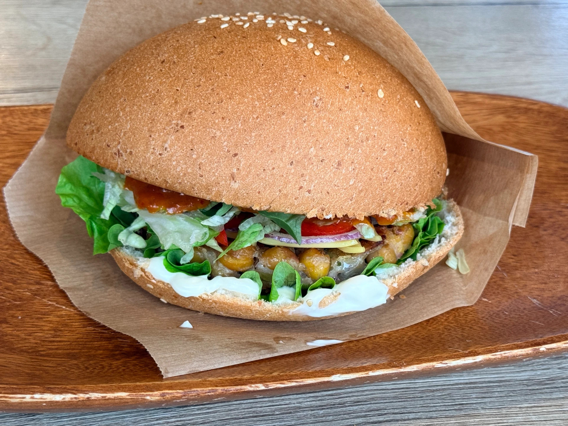 Veganer Burger mit Salat, Paprika und cremiger Sauce auf einem Holzteller