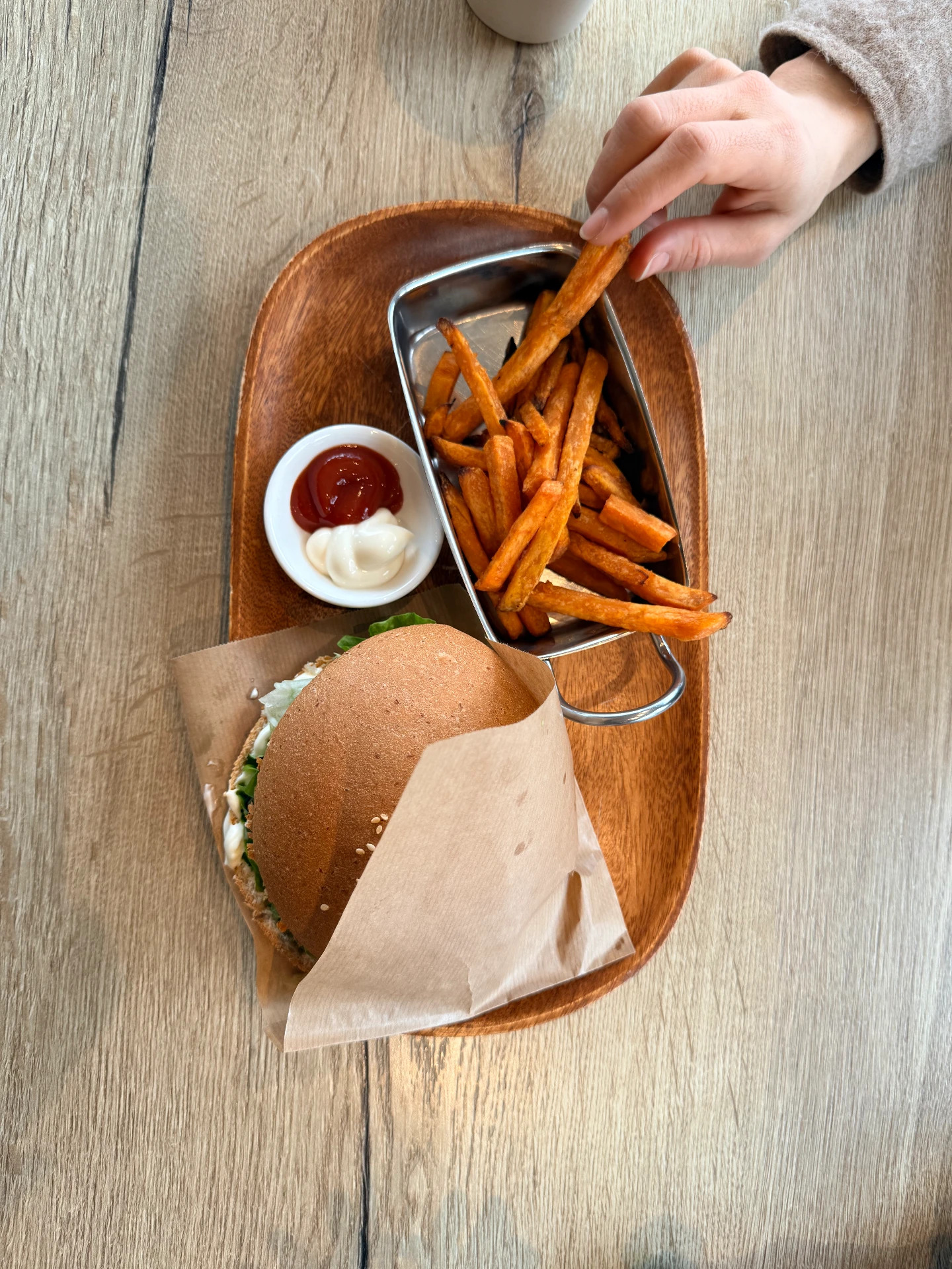 Veganer Burger mit Süßkartoffel-Pommes, Ketchup und Mayo auf einem Holztablett